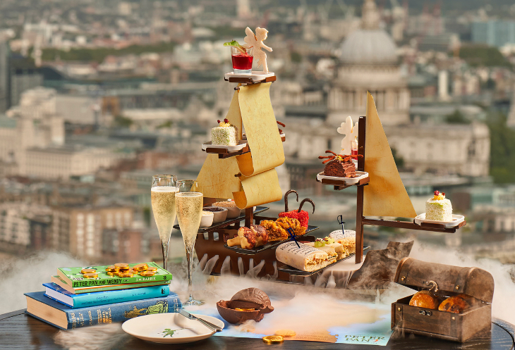 Themed afternoon tea London: a stand shaped like a pirate ship filled with sandwiches and cakes. There are glasses of champagne on the table, and the window offers views over London, including St Paul's Cathedral.