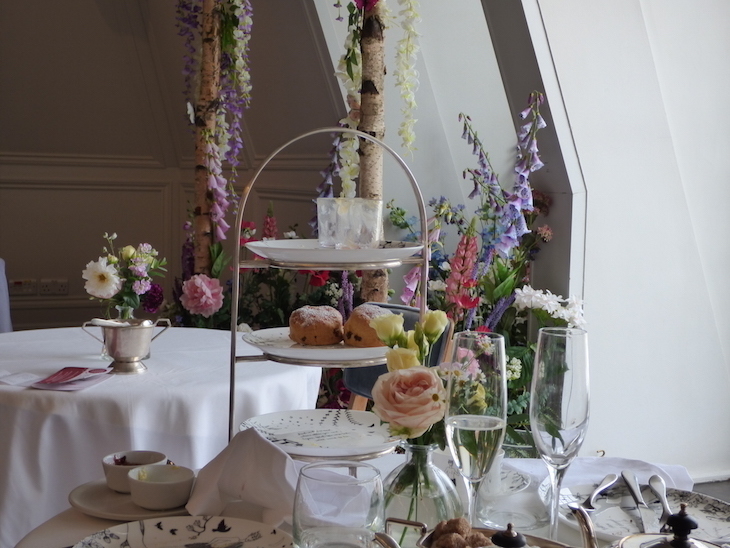 Themed afternoon teas London: An afternoon tea stand against a backdrop of pastel-coloured flowers.