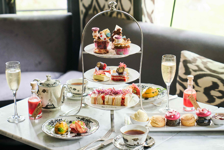 Themed afternoon tea London: a simple tiered stand on a table, with sandwiches and Alice in Wonderland themed cakes, topped with crowns, mushrooms and playing cards.