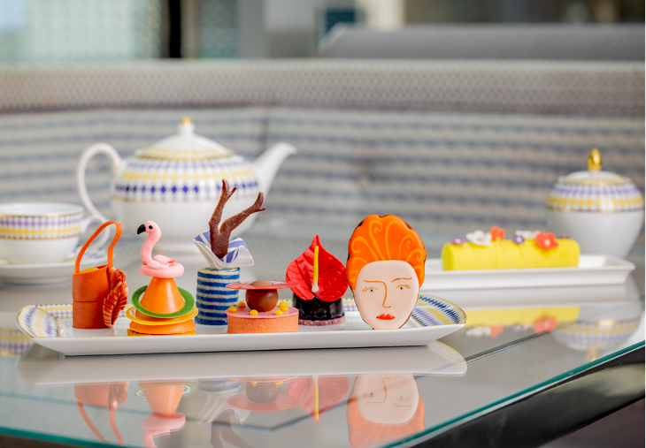 Themed afternoon tea London: a plate with six colourful cakes representing different fashion items, including a handbag, and a biscuit depicting Vivienne Westwood's face.